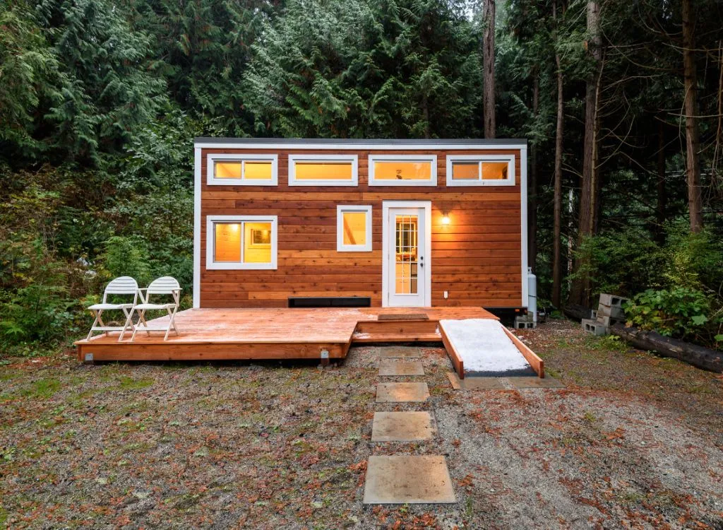 A small wooden ADU (Accessory Dwelling Unit) sits in front of a verdant forest