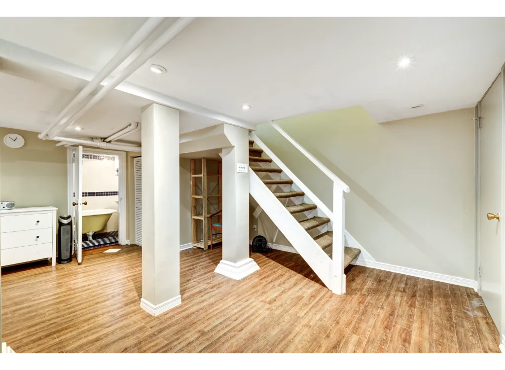 A A basement with a wooden floor with a staircase that leads upstairs.